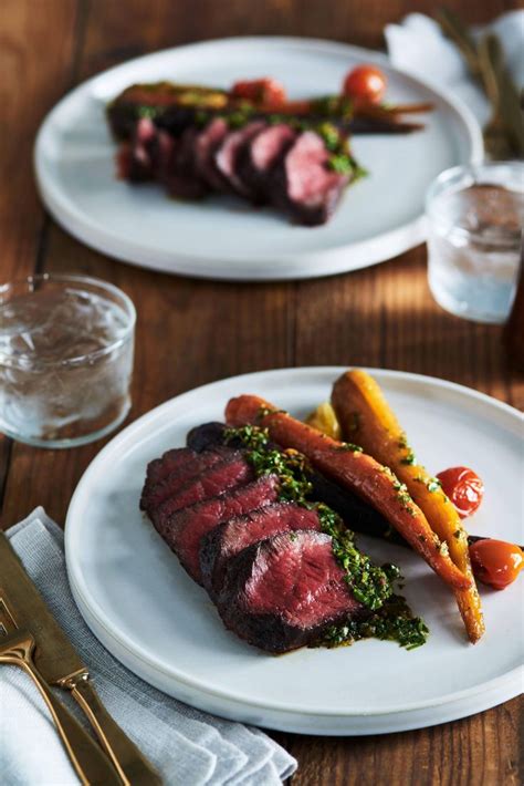 Two White Plates Topped With Meat And Veggies On Top Of A Wooden Table