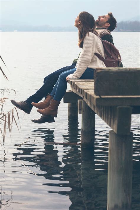 Closeup Of Young Couple Sitting On Wooden Dock At The Lakeshore By