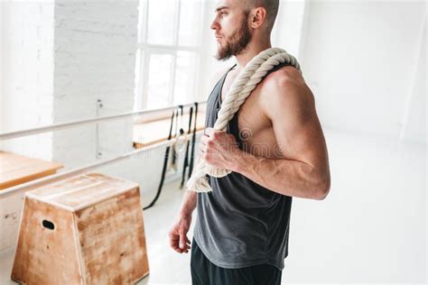 Muscular Man Holding Gymnastic Rings At Light Gym And Looking Away