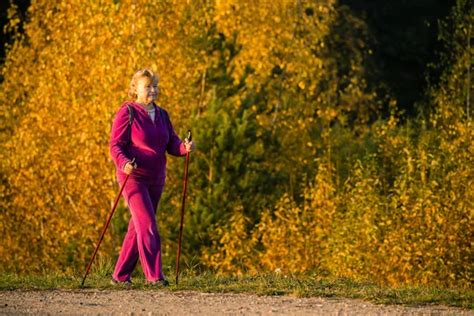 Senior Woman Nordic Walking With Sticks In The Countryside Outdoors