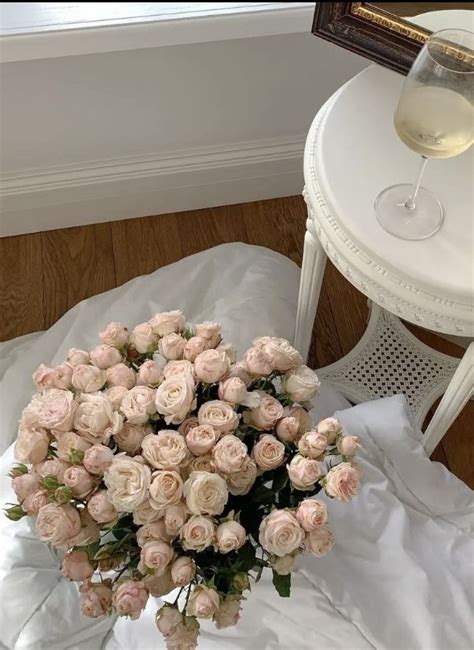 A Bouquet Of Pink Roses Sitting On Top Of A Bed Next To A Glass Of Wine