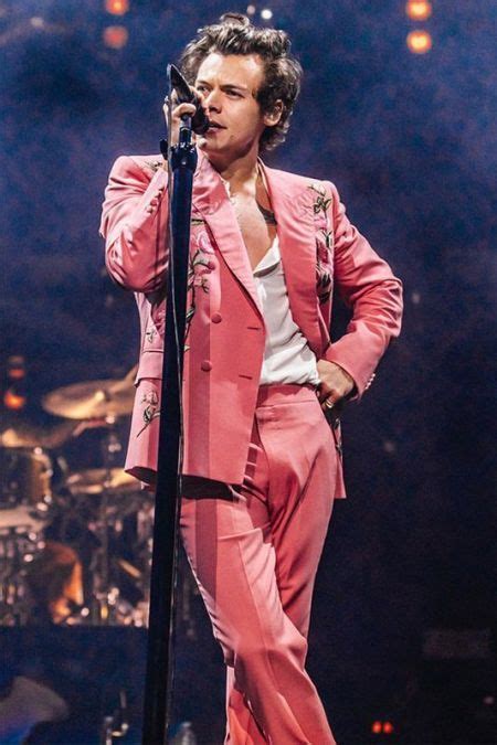 A Male In A Pink Suit And White Shirt Is Holding A Microphone On The Stage