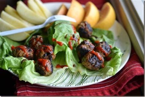 A Plate With Meatballs And Lettuce On It Next To Some Fruit Slices