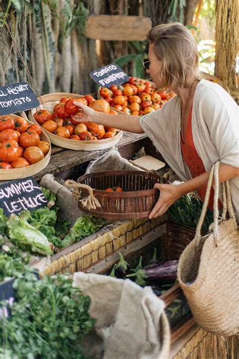 A Woman Is Shopping For Fresh Produce At A Farmers Market With Her Hands In The Basket