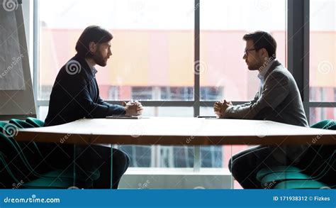 Two Businessmen Sitting Opposite At Table Confrontation And