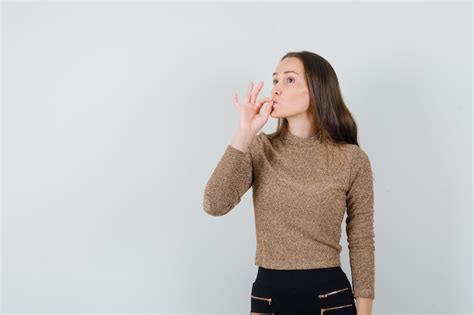 골드 도금 한 스웨터와 검은 색 바지에 맛있는 제스처를 보여주는 젊은 여자와 낙관적 찾고 전면보기 무료 사진