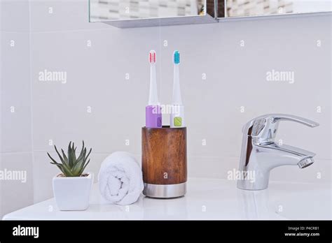 Two Electric Toothbrushes In Wooden Glass On Sink In The Bathroom With