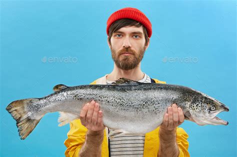 Horizontal Portrait Of Successful Angler With Beard Holding Huge Fish