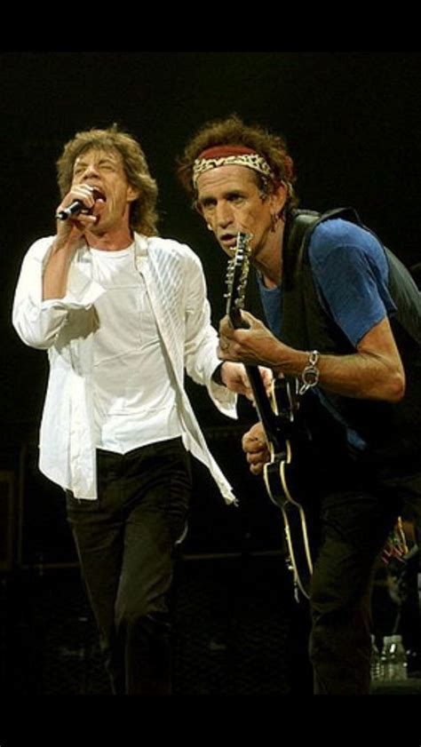 Two Men On Stage Singing Into Microphones With One Holding An