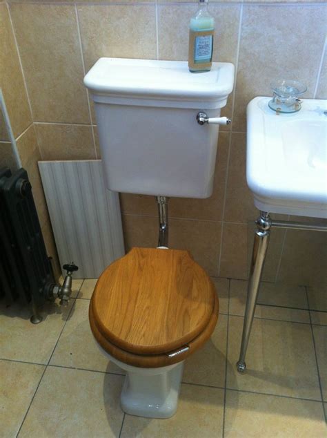 A Wooden Toilet Seat In A Bathroom Next To A White Sink And Radiator