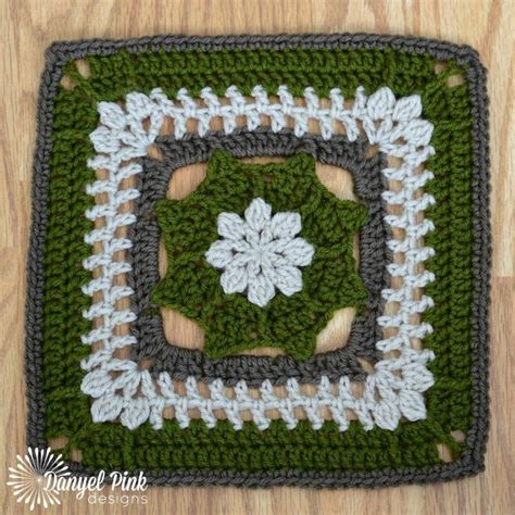 A Crocheted Square With White Flowers In The Center On A Wooden Floor