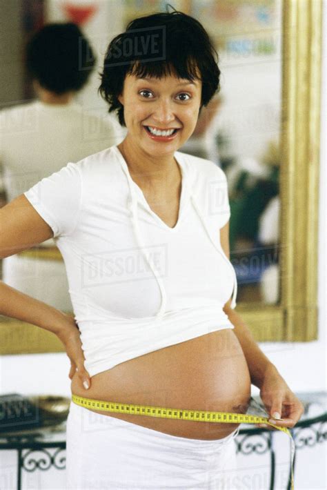 Pregnant Woman Measuring Stomach With Measuring Tape Smiling At Camera