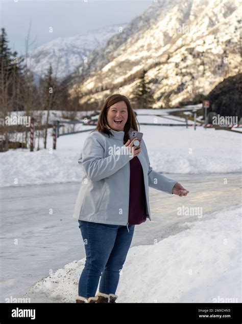 A Caucasian woman holding cell phone and snow standing on icy road in ...