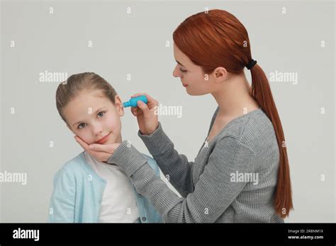 Mother Dripping Medication Into Daughters Ear On Light Grey Background