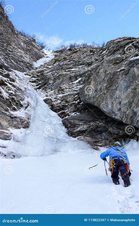 Male Ice Climber Approaches A Long And Steep Waterfall In A Narrow