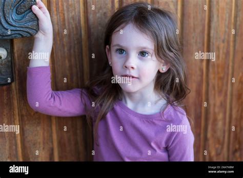 A Cute Blonde Girl In A Purple T Shirt Stands Smiling Near The Wooden Door Of Her House Happy