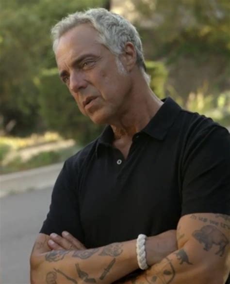 A Man With Grey Hair And Tattoos On His Arms Standing Next To A Street