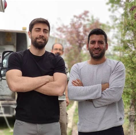 Two Men Standing Next To Each Other In Front Of A Truck With Their Arms