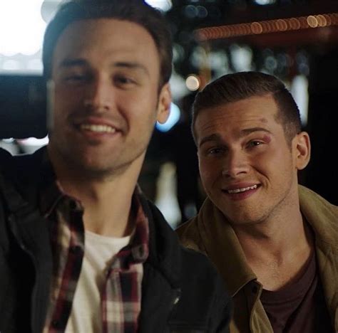 Two Men Sitting Next To Each Other In Front Of A Bar Smiling At The Camera