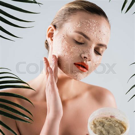 Naked Woman Applying Scrub And Holding Container Near Palm Leaves On