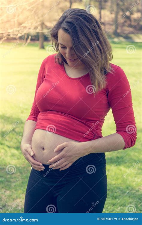 Pregnant Woman Wearing Red Shirt Gently Caressing Her Belly Stock