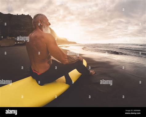 Happy Fit Senior Man Sitting On Surfboard Watching Sunset Time Mature