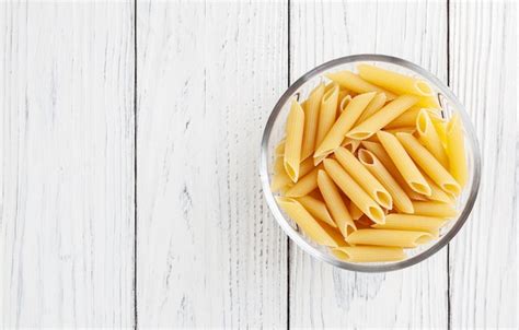 Premium Photo Uncooked Penne Pasta In Glass Bowl On White Wooden