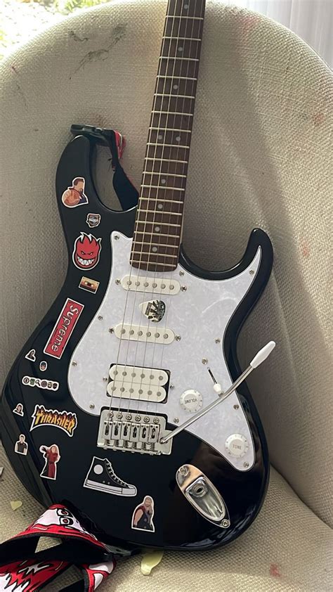 An Electric Guitar With Stickers On It Sitting In A Chair Next To A Remote Control