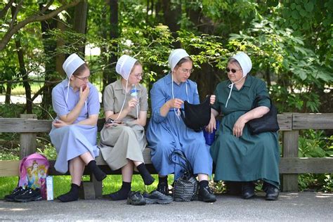 Four Women Are Sitting On A Bench In The Park One Is Holding A Water