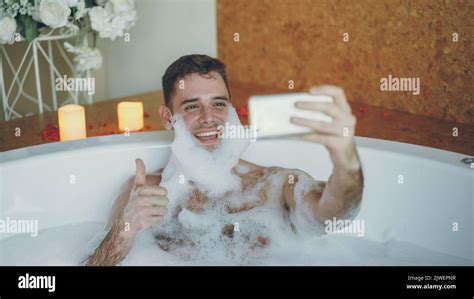 Handsome Cheerful Guy Is Taking Selfie In Bathtub With Soap Foam On His Beard Using Smart Phone