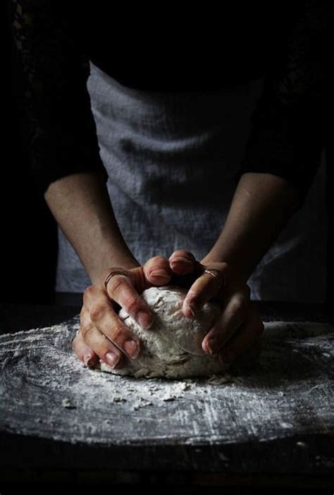 A Person Kneading Dough On Top Of A Wooden Table In Front Of A Black