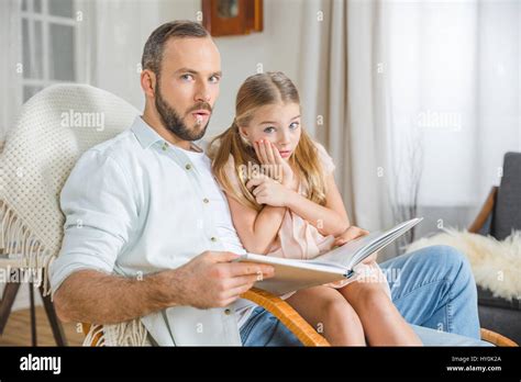 Scared Father And Daughter Sitting In Rocking Chair And Reading Book