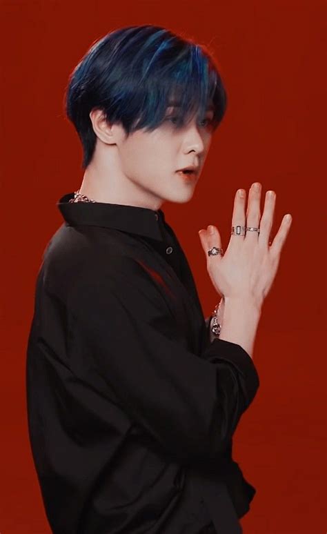 A Man With Blue Hair And Black Shirt Holding His Hands Together