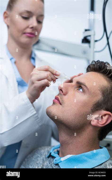 Optometrista hembra poniendo gotas en los ojos del paciente Fotografía