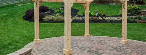 A Wooden Gazebo Sitting On Top Of A Brick Patio Next To A Lush Green Field