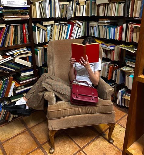 A Woman Is Sitting In A Chair Reading A Book And Holding A Red Bag Over