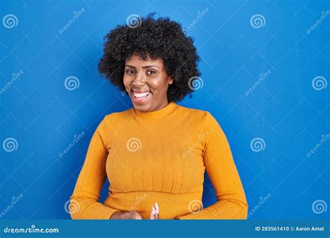 Black Woman With Curly Hair Standing Over Blue Background With Hands Together And Crossed