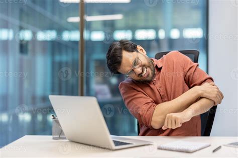 Man in office showing discomfort, experiencing arm pain while seated at