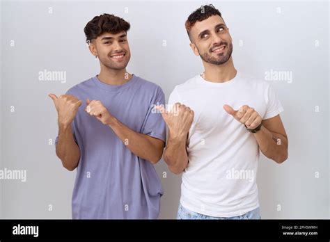 Homosexual Gay Couple Standing Over White Background Pointing To The Back Behind With Hand And