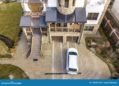 New White Car Parked In Paved Driveway With Green Lawn Decorative Bushes And Brick Fence Of Big