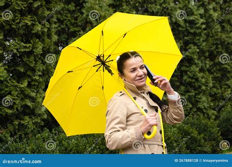 Happy Senior Woman In Yellow Rain Coat With Yellow Umbrella Is Talking