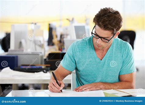 Man Writing At Desk In Busy Creative Office Stock Photo - Image: 29482924