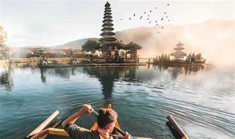 A Man Rowing A Boat On Top Of A Lake With Pagodas In The Background