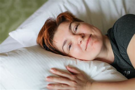 Close Portrait Of Redhead Relaxing Sleeping Adult Woman Lies In White Bed And Smiles At Camera