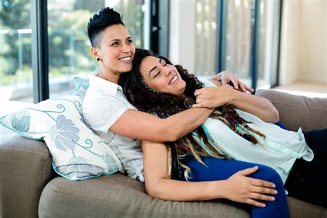 Smiling Lesbian Couple Embracing And Relaxing On Sofa Stock Photo