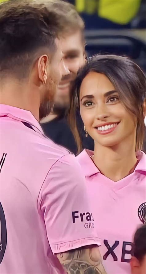 A Man And Woman In Pink Shirts Standing Next To Each Other At A Soccer Game