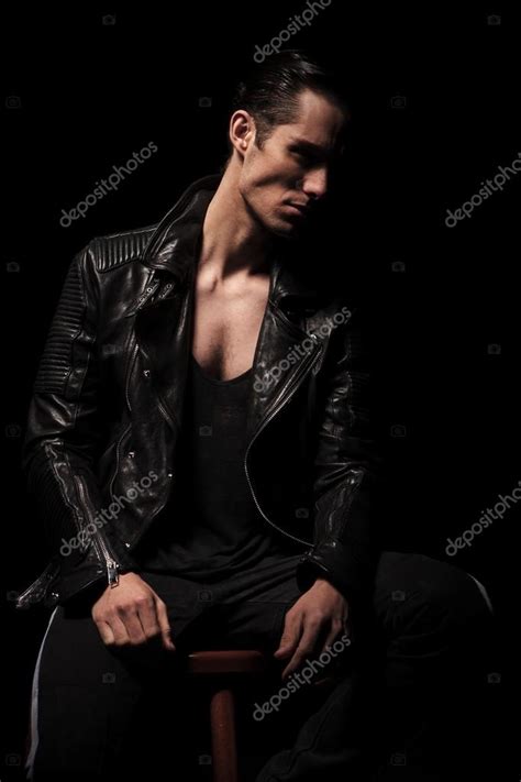 Rocker in black leather jacket posing seated in dark studio Stock Photo ...