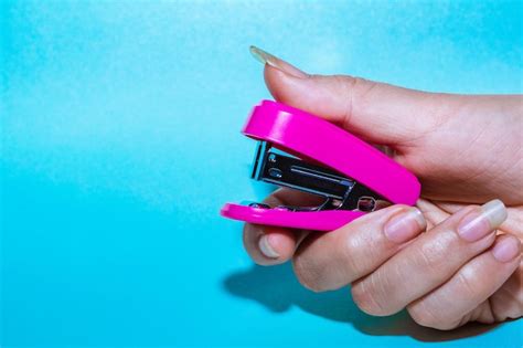 La mano de una joven latina con uñas largas sosteniendo una pequeña grapadora rosa a punto de