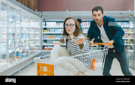 At The Supermarket Man Pushes Shopping Cart With Woman Sitting In It