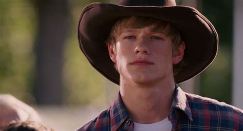 A Young Man Wearing A Cowboy Hat And Looking Off Into The Distance With Other People In The